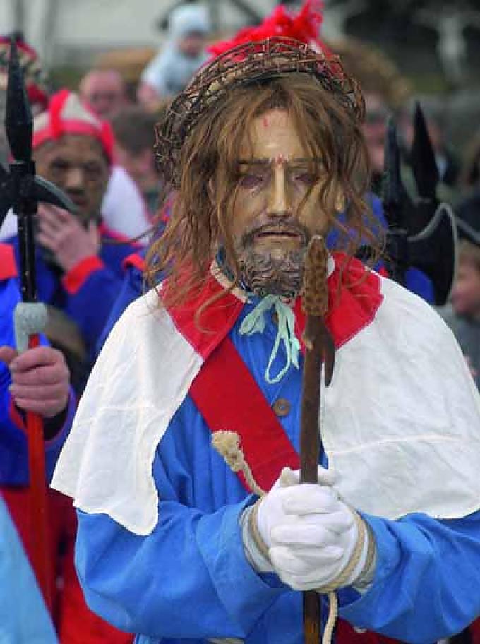 Christus. Jesus und seine Lieblingsapostel, alle maskiert, vor dem Ulrichskirchlein in Tresdorf. Im Vordergrund ein großes Kruzifix.