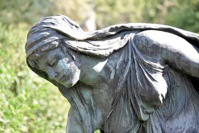 Figur eienr Trauernden an einem Grab Herz auf einem Baumstamm.