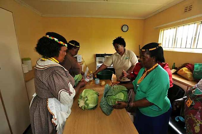 Die Frauen des „Old Age Center“ in Ilitha kochen Gemüse unter Anleitung ihrer Lehrerin Koleka Ralo (3.v.l.)