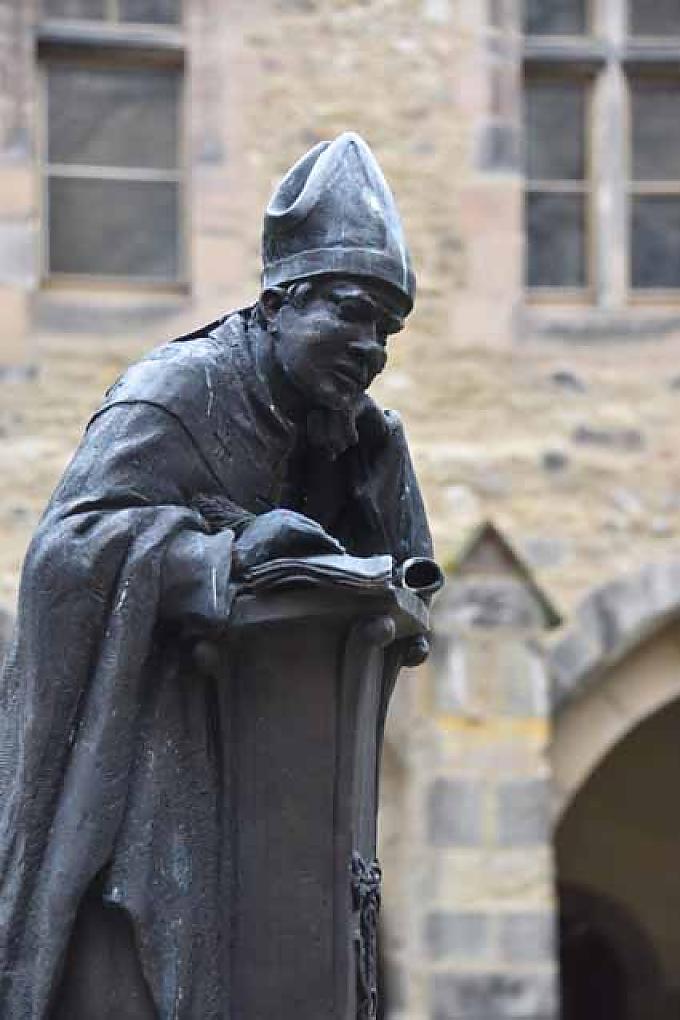 Innmitten des Thietmarbrunnens stützt er sich sinnierend mit den Ellenbogen auf ein Schreibpult und schaut dabei auf den Dom. Innmitten des Thietmarbrunnens stützt er sich sinnierend mit den Ellenbogen auf ein Schreibpult und schaut dabei auf den Dom.