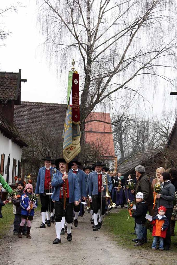 Ankunft der Trachten-Musikgruppe, gefolgt vom Pfarrer und den Ministranten Kinder warten mit ihren Palmen