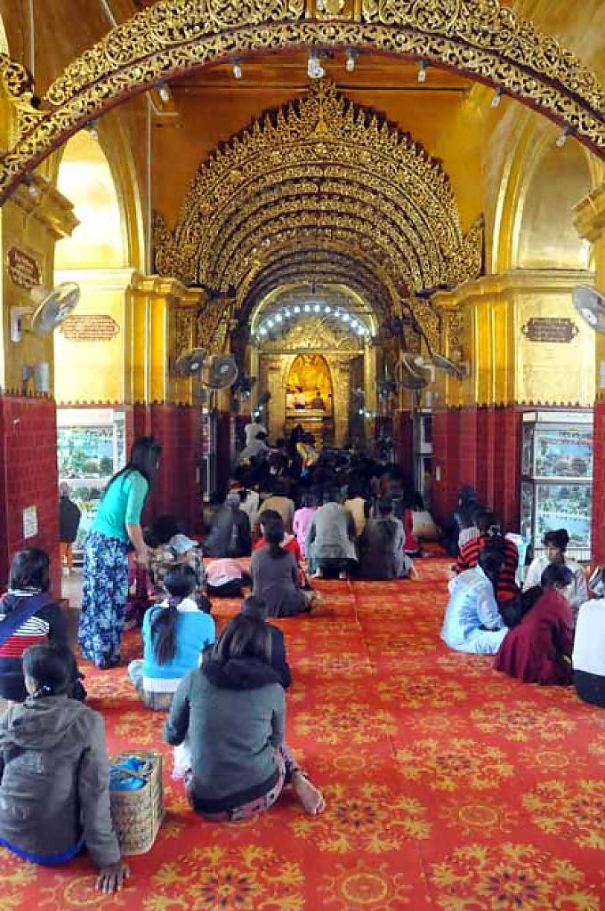 Frauen sitzen betend vor der Figur. Sie dürfen nicht eigenhändig das Gold auftragen Gläubige tragen Blattgold auf die Figur des goldenen Buddhas auf