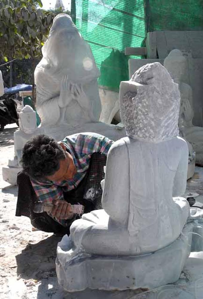 Ein Mann meißelt an der Figur eines Buddhas Gläubige tragen Blattgold auf die Figur des goldenen Buddhas auf