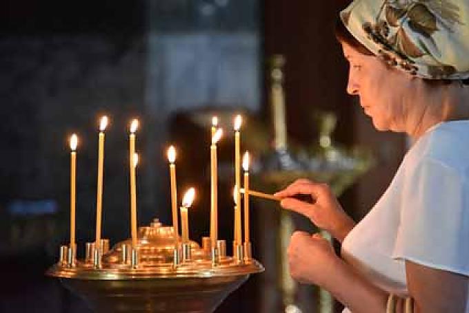 Eine Frau entzündet eine Kerze vor einer Ikone Glockenturm und Uspenski-Kathedrale.
