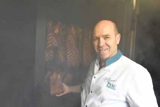 Frank Pfau kontrolliert den Räucherofen. Frank Pfau schneidet einen Schinken an.