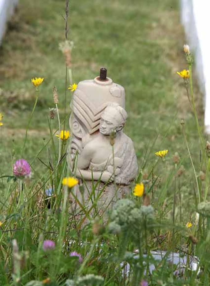 Die Figur eines Maoris mit einer flachen Handkeule „Patu“ in der Hand steht im tiefen Gras. Maorisymbol für ewige Verbundenheit und Liebe.