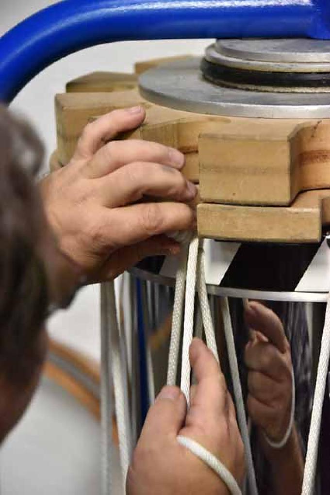 Vor dem Schränkbock hockt sich Büchner auf einen niedrigen Stuhl, lockert noch einmal die Muskeln und beginnt dann damit, die Seile einer Trommel nachzuspannen. Walter Büchler fährt mit dem Finger über die Kante und schaut prüfend durch den zukünftigen Trommelkörper.