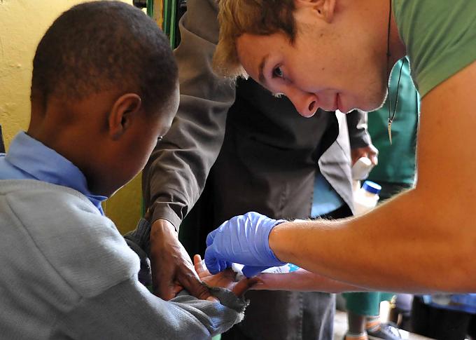 Felix versorgt kleine und größere Wunden. Erwartungsvoll schauen die Schulkinder zu Felix hinab.