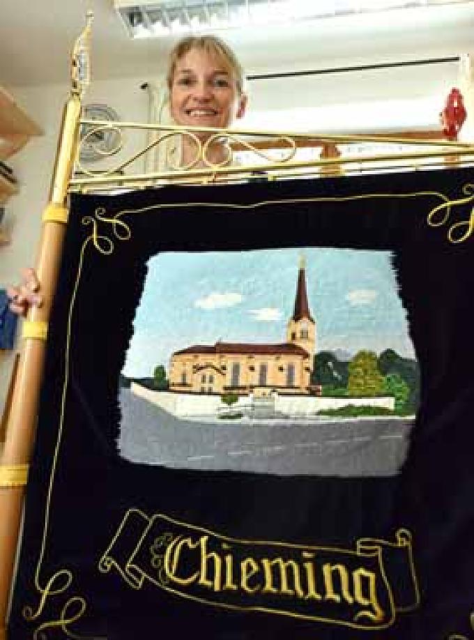 Stolz präsentiert Irmi Axmann die Fahne mit der Darstellung der Kirche in Chieming. Die Gemeinde im oberbayerischen Landkreis Traunstein liegt am Ostufer des Chiemsees. Irmi Axmann in ihrer kleinen Werkstatt.