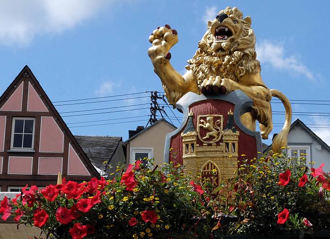 Golden blitzt der zweischwänzige Löwe im Sonnenlicht und wacht über das bunte Treiben auf dem Marktplatz