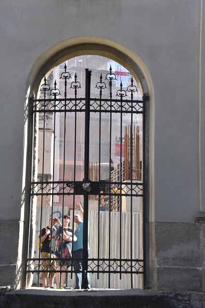 Passanten blicken durch das Gitter des Tores in den Innenhof