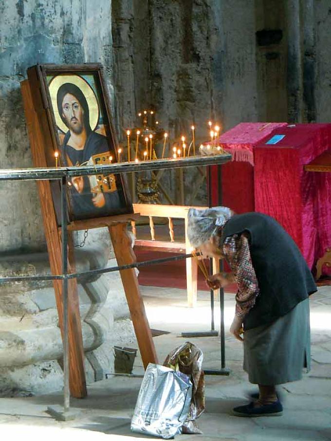 Alte Frau betet in Alaverdi-Kathedrale. Kaukasus. Kazbegi. Dreifaltigkeitskirche (14.Jh.) auf 2200m, dahinter Mount Kazbegh, 5047m.