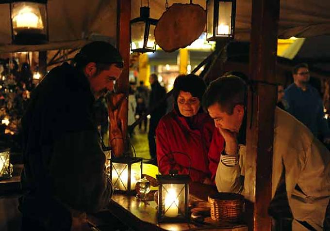 Nur mit Kerzen und Fackeln werden die Stände erleuchtet. Eine mittelalterlich gekleidete Frau legt Holz auf ein Feuer