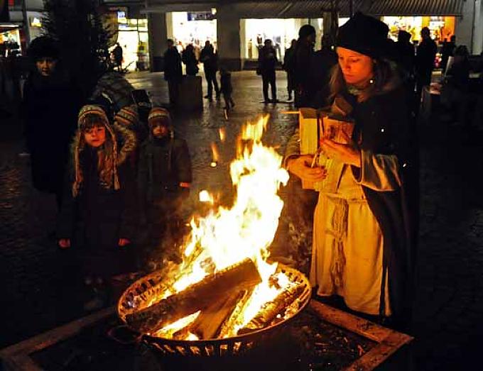 Eine mittelalterlich gekleidete Frau legt Holz auf ein Feuer Eine mittelalterlich gekleidete Frau legt Holz auf ein Feuer