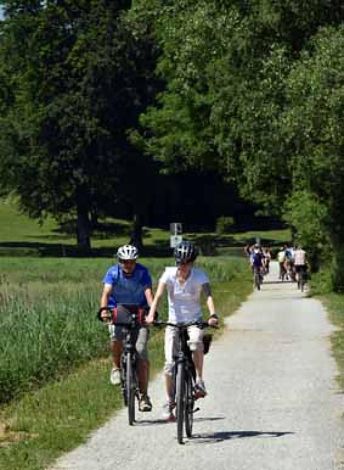 Fahrradfahrer unterwegs Kaum auf dem Sattel, müssen die Radler auf ihrer Tour auch schon den ersten Halt einlegen. Denn quietschend und große Qualmwolken gen Himmel hinauf ausstoßend, stampft eine historische Dampflok im bayerischen Prien quer über die Fahrbahn.