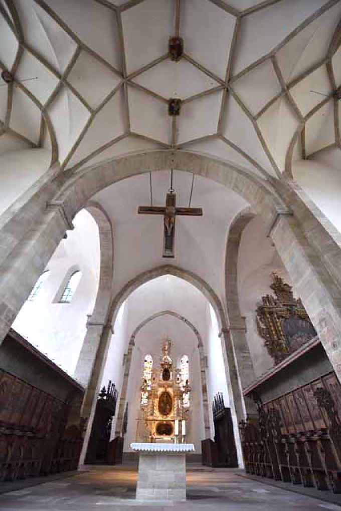 Blick durch das Mittelschiff des Merseburger Doms zum Hochaltar. Innmitten des Thietmarbrunnens stützt er sich sinnierend mit den Ellenbogen auf ein Schreibpult und schaut dabei auf den Dom.