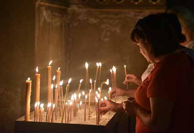 Kerzen werden vor einer Ikone entzündet. Der schummerige Innenraum wird nur von Fenstern im Chor erhellt, zudem von den vielen hundert Kerzen, welche die Gläubigen aufstellen.