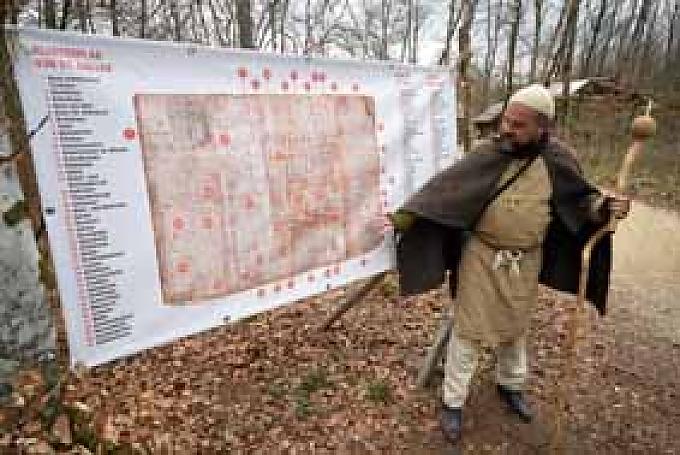 Matthias Hofmann, Führer der Besuchergruppe. Gruppe vor einer Tafel mit dem Abbild des St. Gallener Klosterplans. Balken werden mit der Axt bearbeitet.