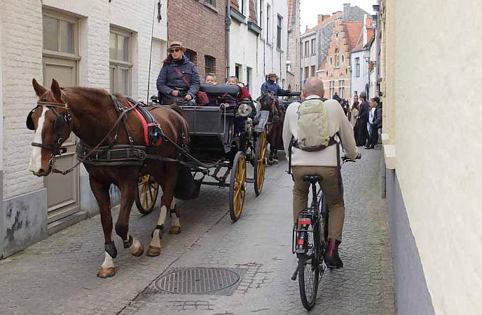 Pferdekutschen, Radfahrer und Fußgänger in einer Gasse in Brügge Pferdekutschen, Radfahrer und Fußgänger in einer Gasse in Brügge